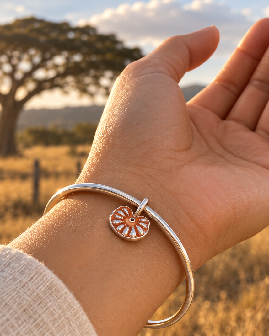 Guanacaste seed charm bracelet in 950 sterling silver, worn on wrist with a guanacaste tree and savanna at sunset