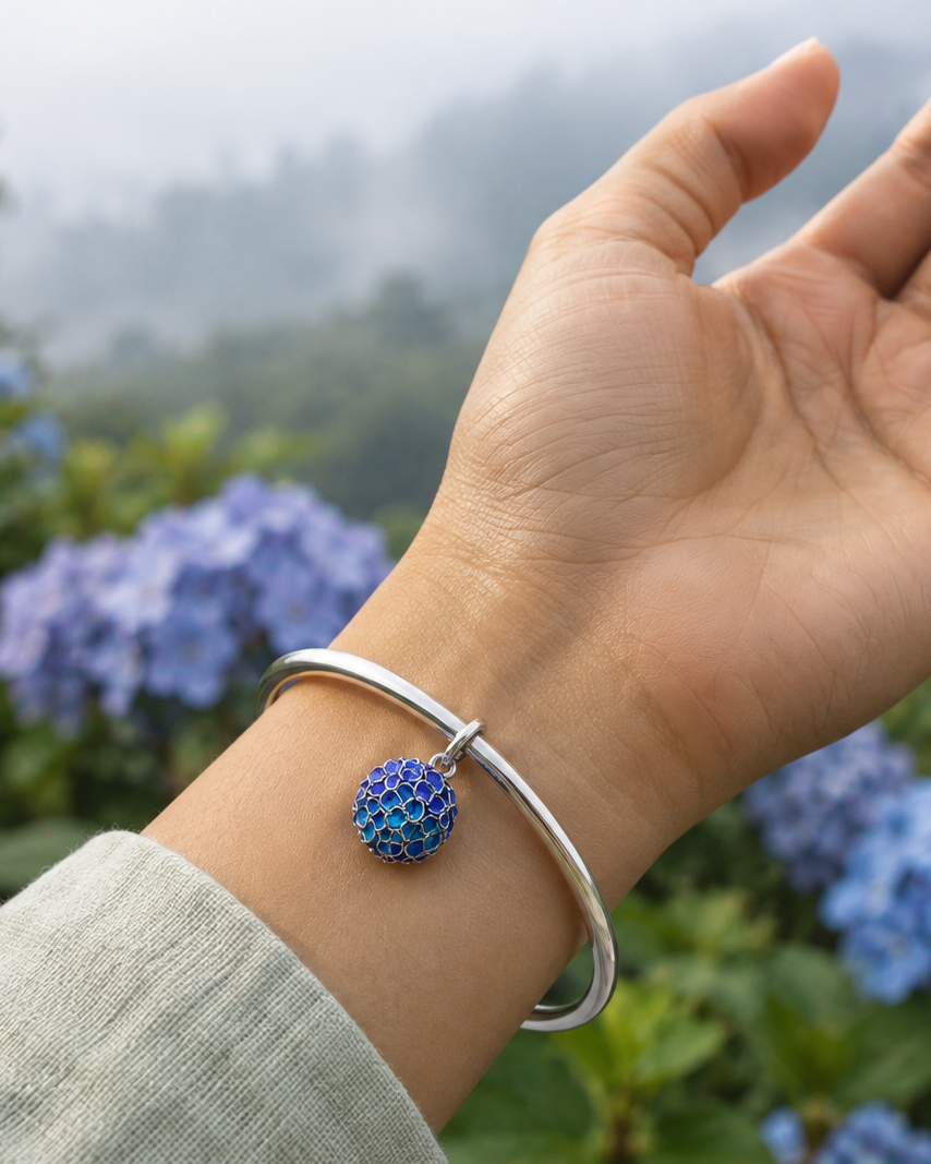 Hydrangea flower pendant necklace in 950 sterling silver, worn close-up with blue hydrangea flowers in the background