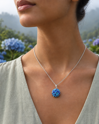 Hydrangea flower pendant necklace in 950 sterling silver, worn close-up with blue hydrangea flowers in the background