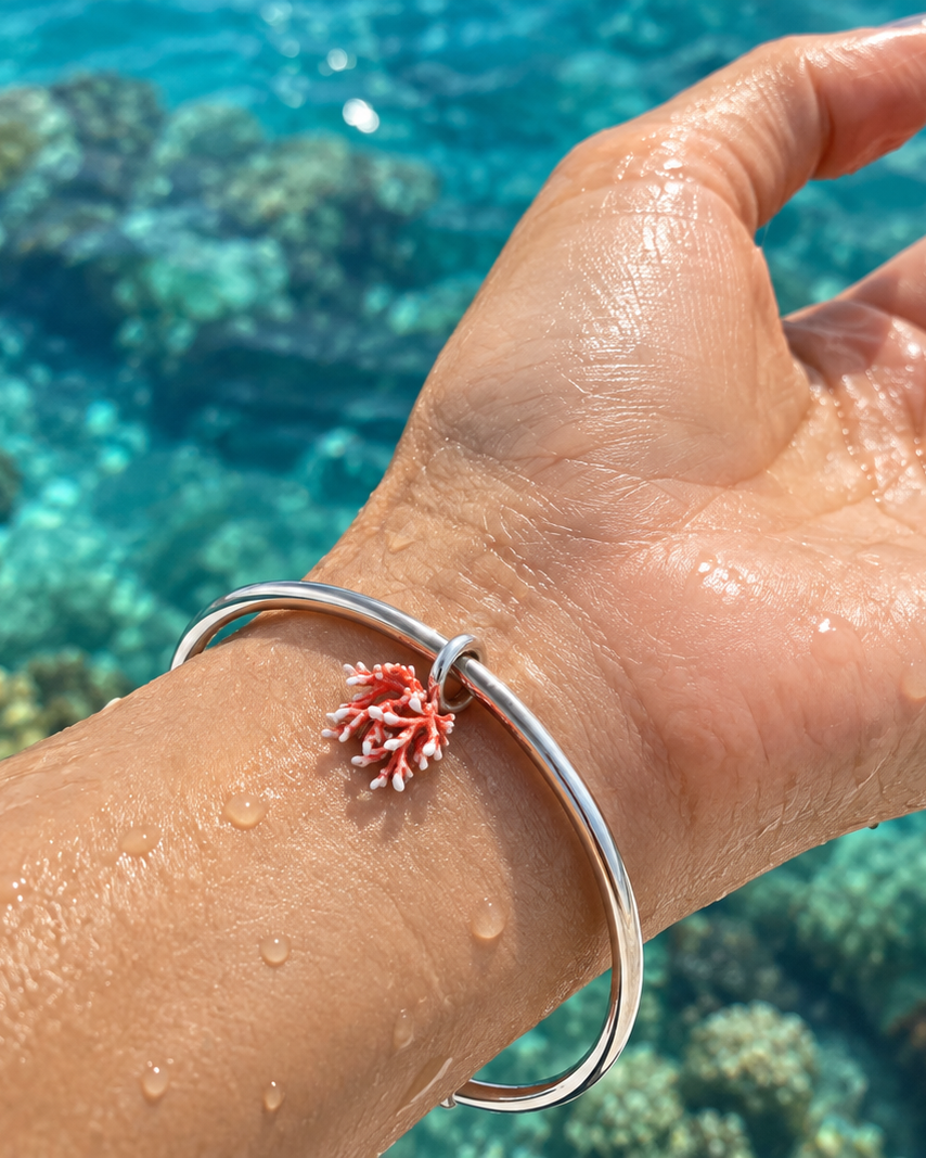 Red coral charm bracelet in 950 sterling silver, worn on wrist with a coral reef background